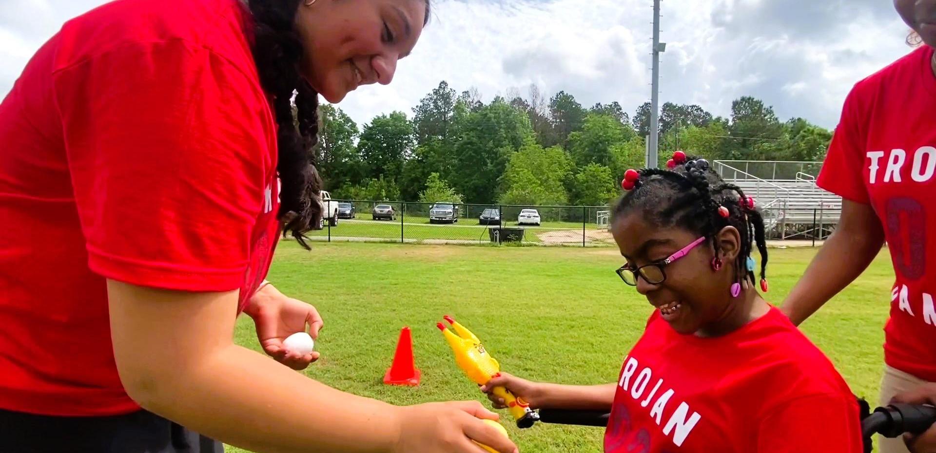 Two students collaborating with a younger child in red shirts on a field.