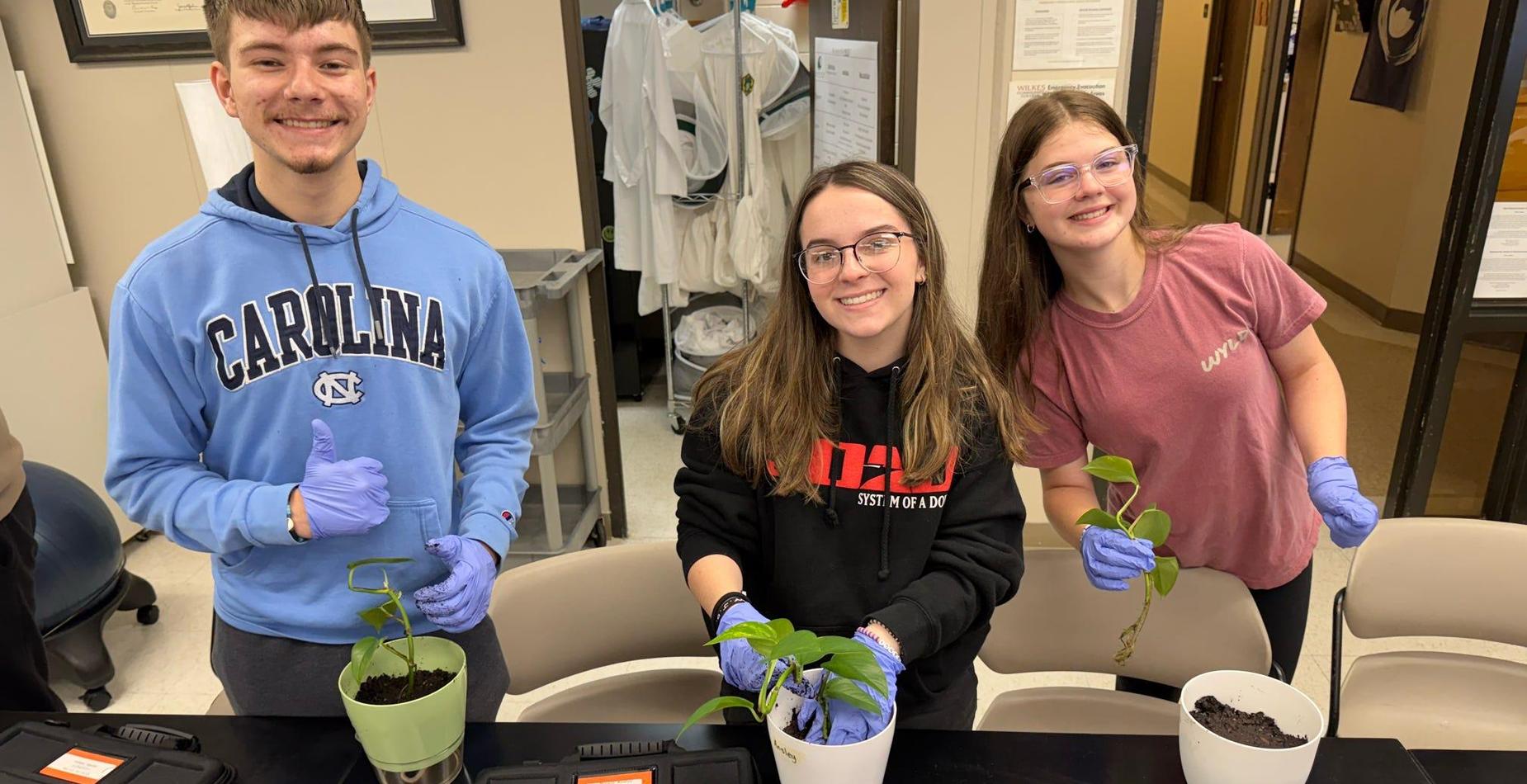 Three students smiling and holding potted plants in Dr. Pipes' Hort class