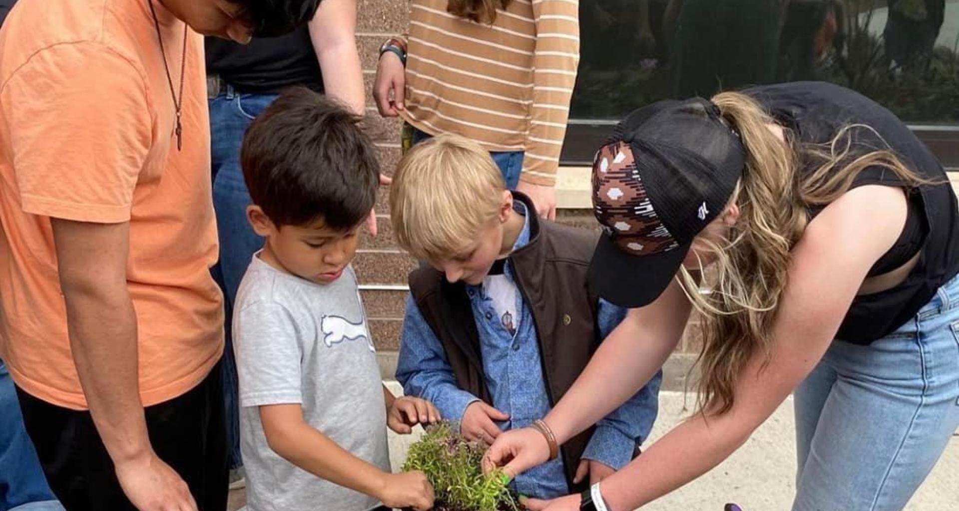 Children and adults gardening together, planting and discussing plants.