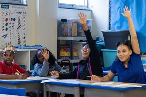 Three students raise their hands with smiles