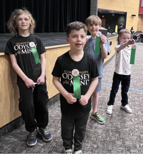 A team of elementary students posing with award ribbons at the Odyssey of the Mind competition.