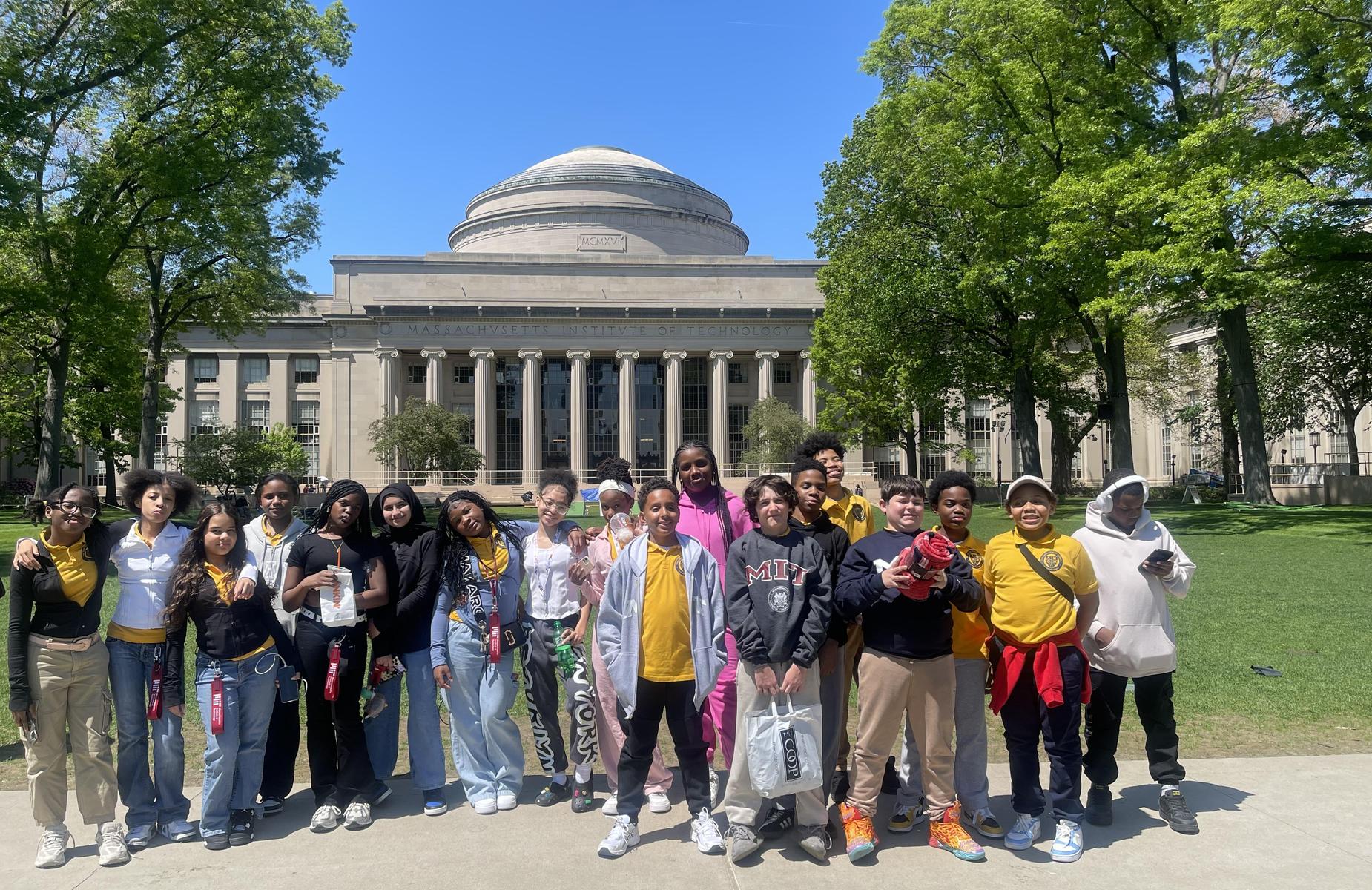 Group of students posing in front of a large academic building under a blue sky.