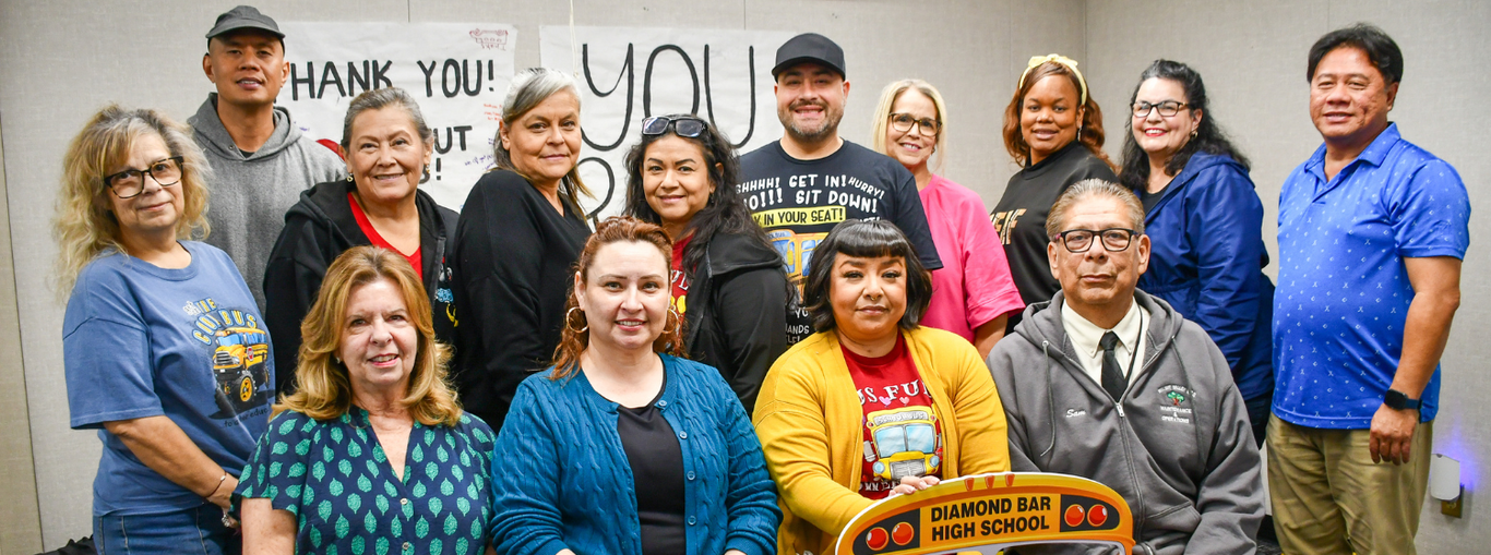 A diverse group of adults gathered together with a sign thanking volunteers at a meeting.