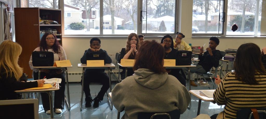 four students sit at desks facing judges