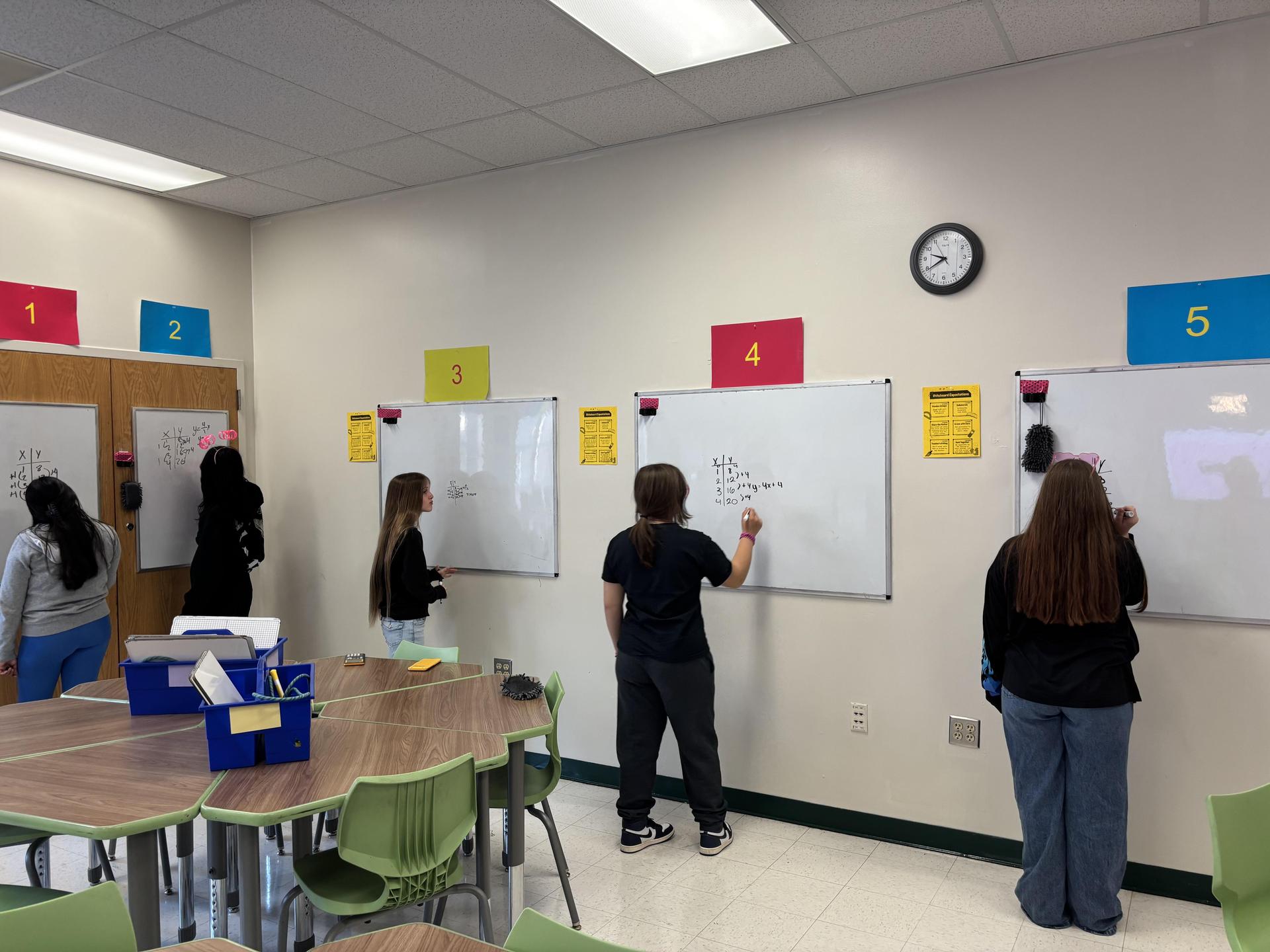Students engaging in math activities at whiteboards in a classroom.