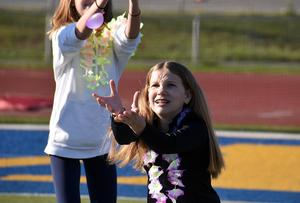 Children wearing leis reach for balloons at a sports field.