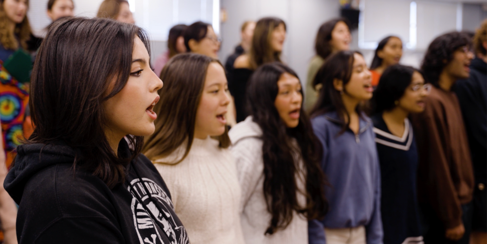 A choir of diverse students singing together in a music classroom.