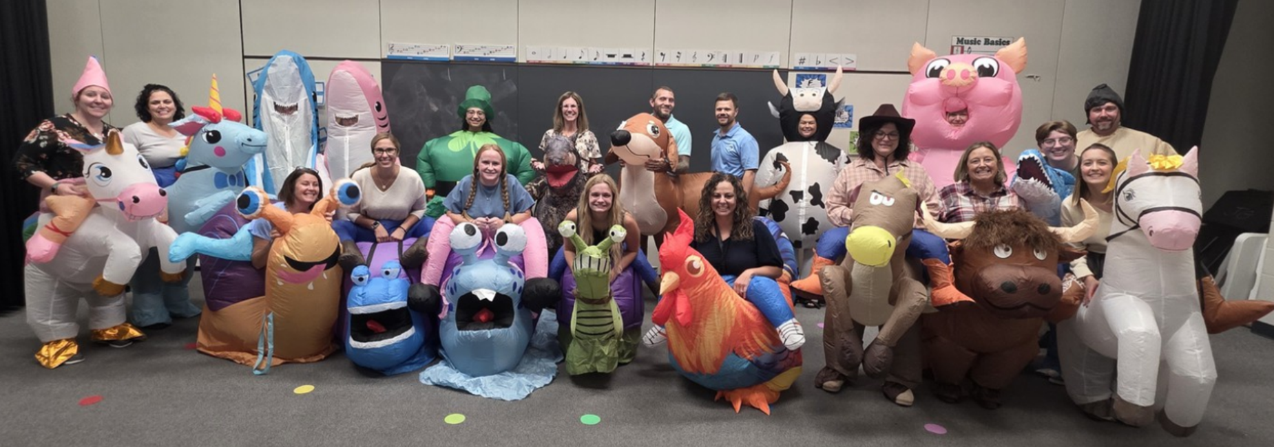 A large group of people in inflatable animal costumes posing together in a classroom.