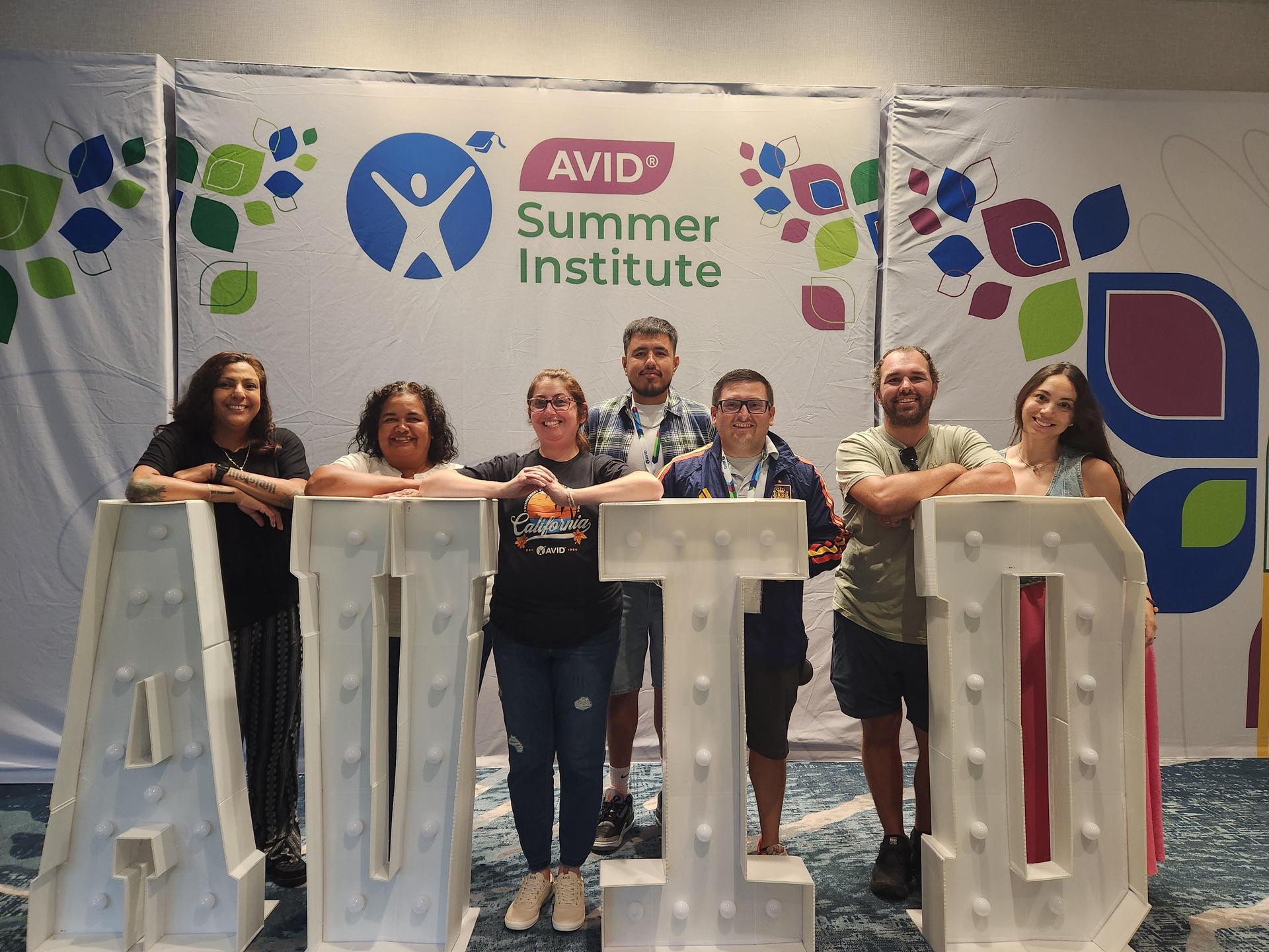 Group of seven people posing behind large letters spelling 'AVID' at an event.