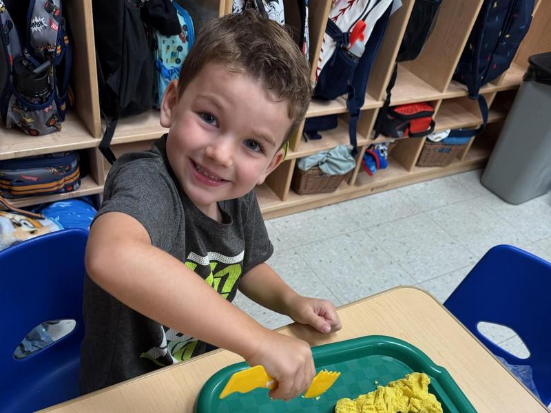 Boy joyfully playing with yellow playdough on a green tray.