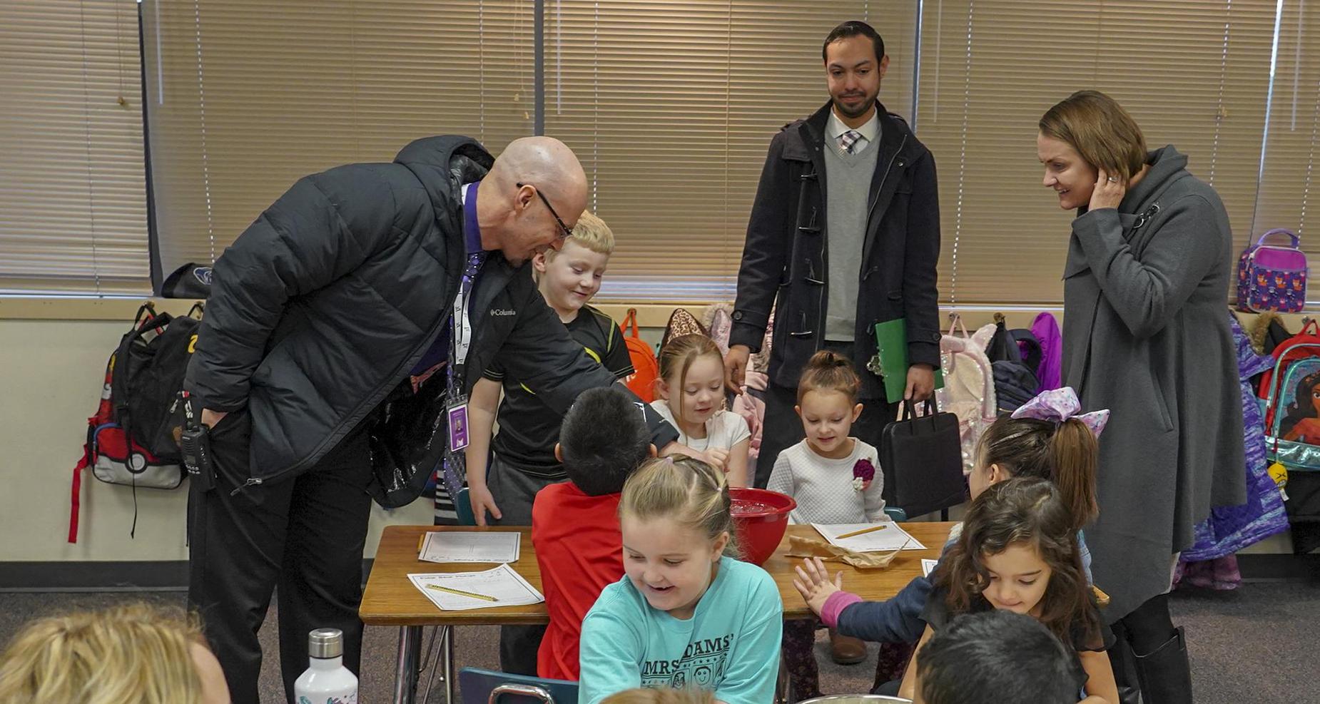 School principal and two guests are in a classroom.