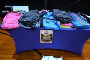 Colorful backpacks arranged on a table with a school sign in the foreground.