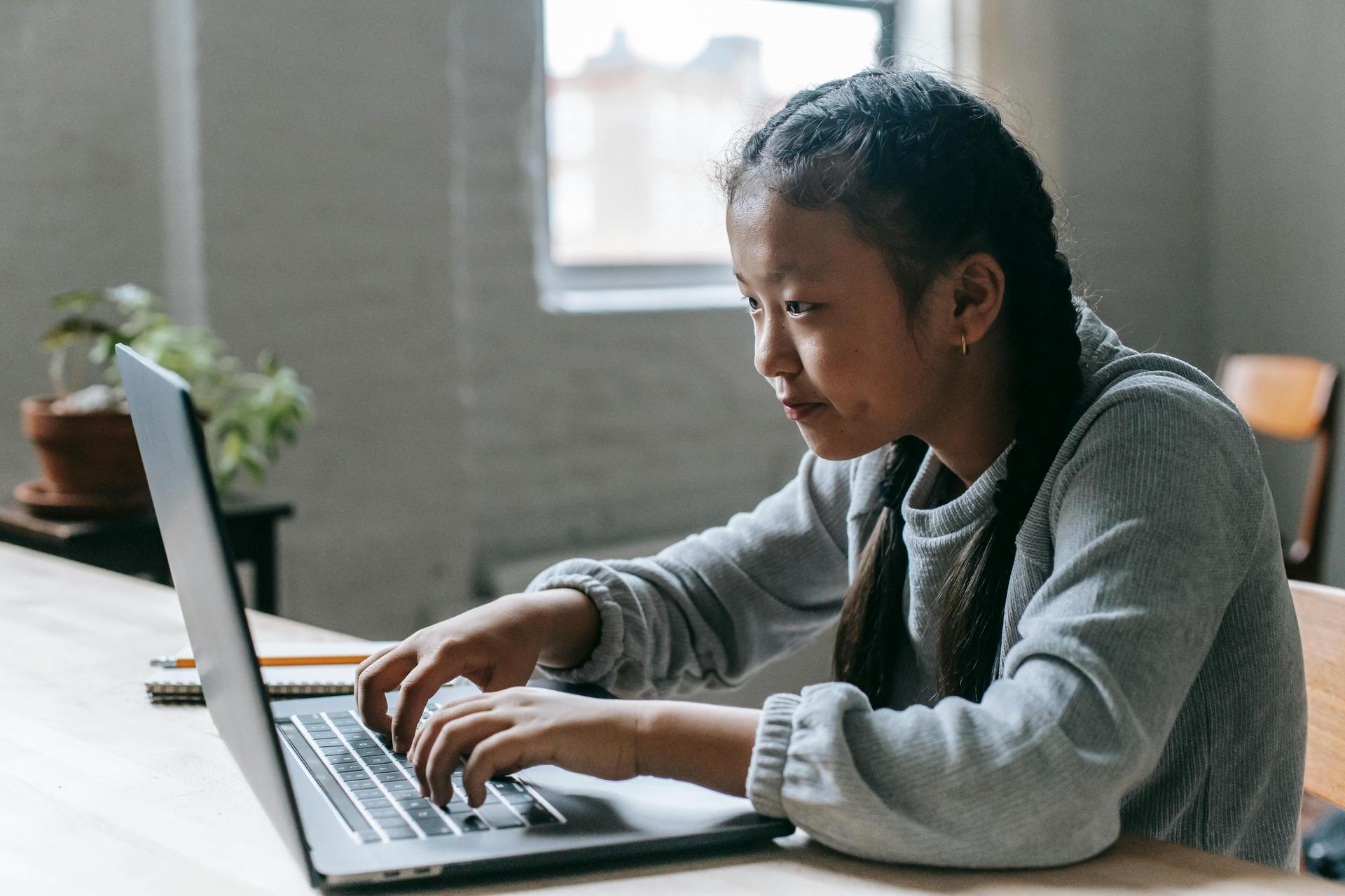 A girl typing on a laptop with a thoughtful expression in a bright room.