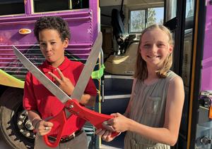 Two students stand with giant scissors at a ribbon cutting