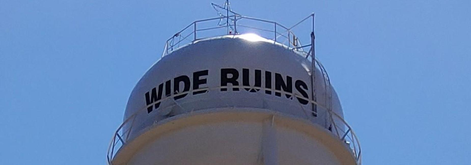 Water tower with the words 'WIDE RUINS!' against a clear blue sky.