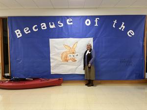A woman stands beside a large blue banner featuring a rabbit and the words 'Because of the.'