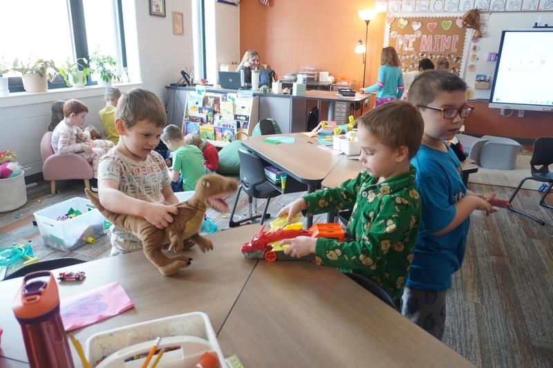 Two students play with a dinosaur and a car carrier.