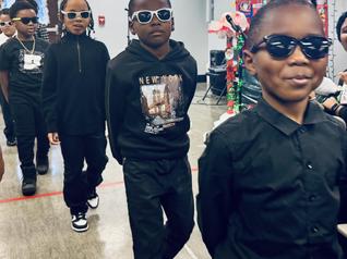 Smiling Black graduate wearing a sash and bow tie, posing proudly at a ceremony.