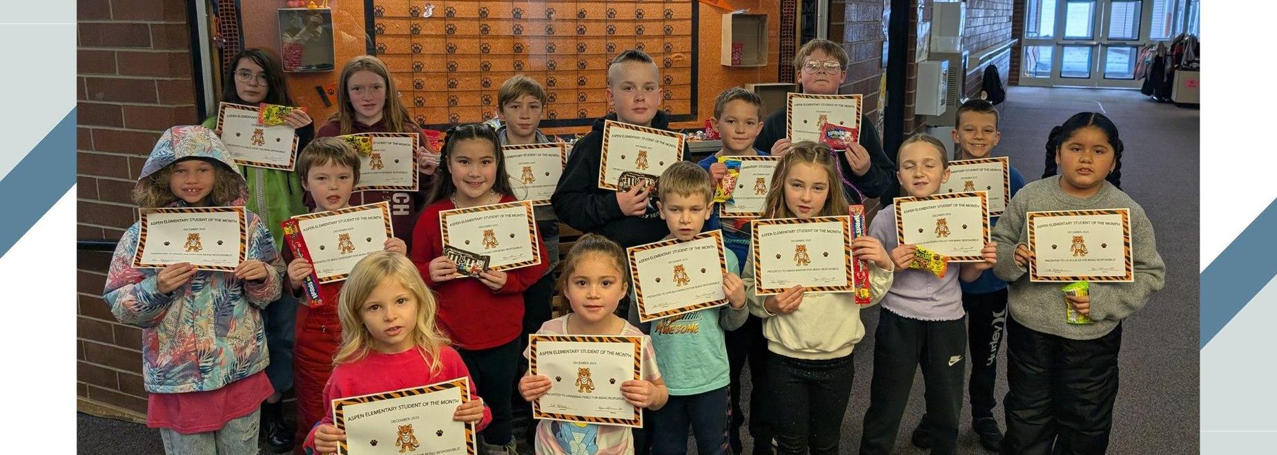 Group of children holding certificates and smiling in a school hallway.