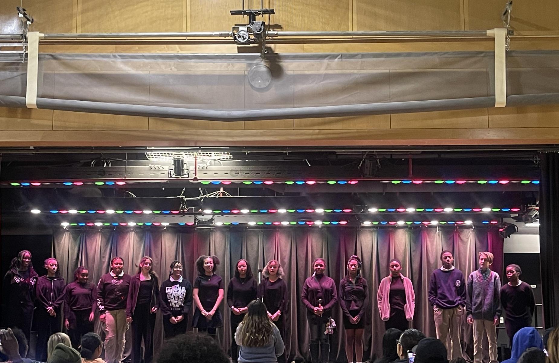 Group of performers on stage during a show with colorful lights.