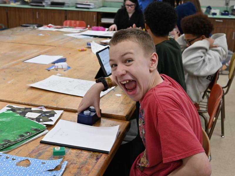 Smiling boy in a classroom, enjoying a project at a table with classmates.