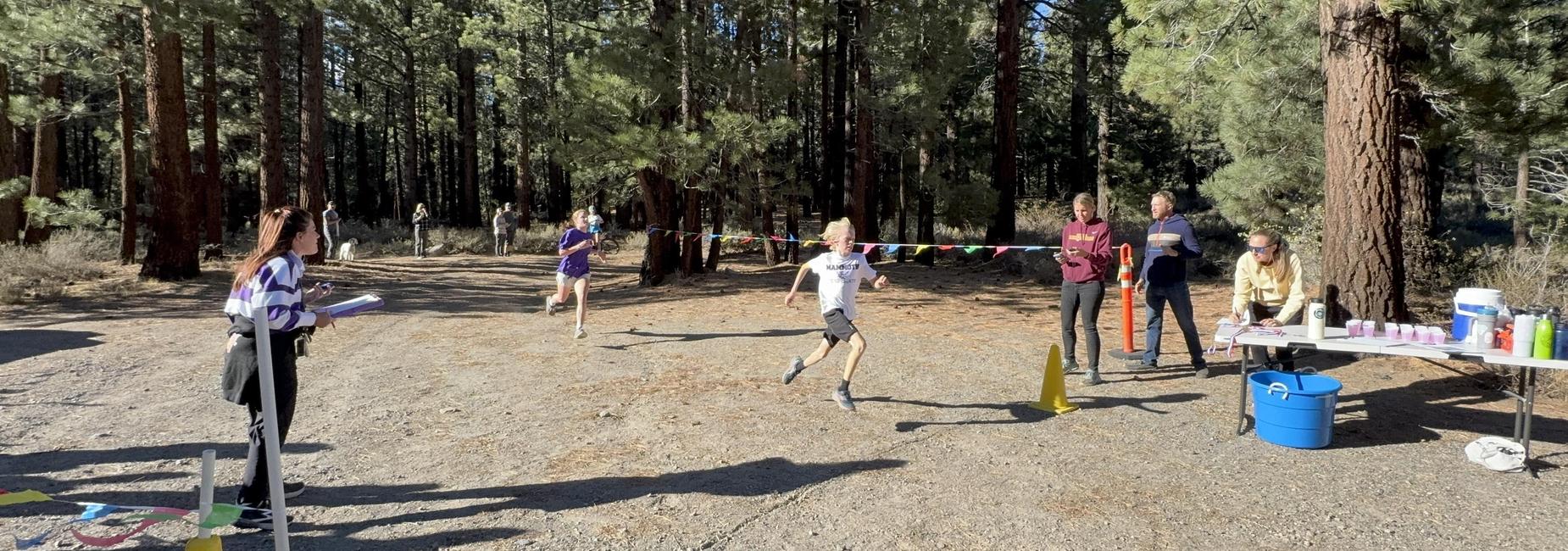 Two runners sprinting towards the finish line with spectators and refreshments nearby.