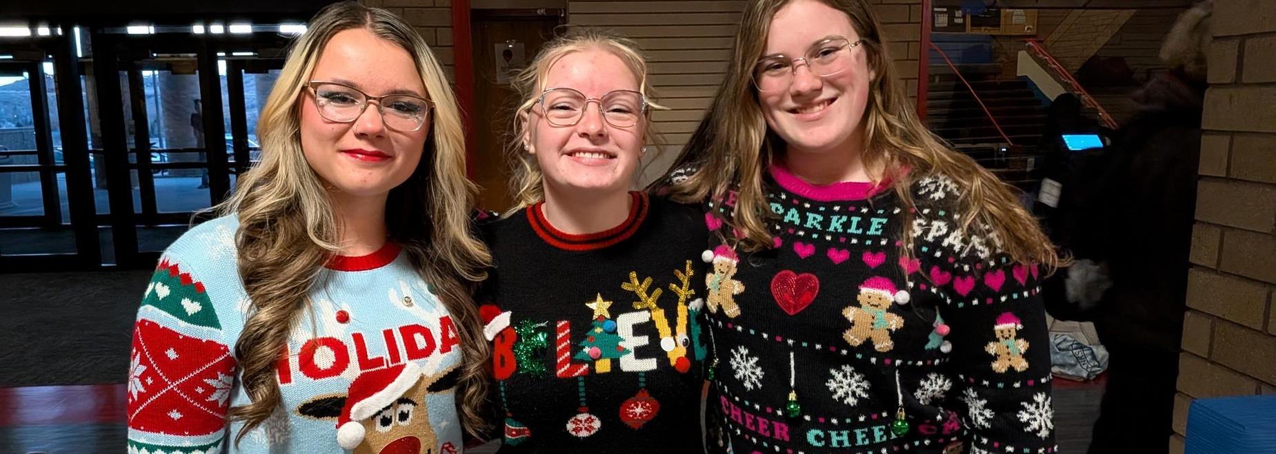 Three women smiling in colorful holiday sweaters.