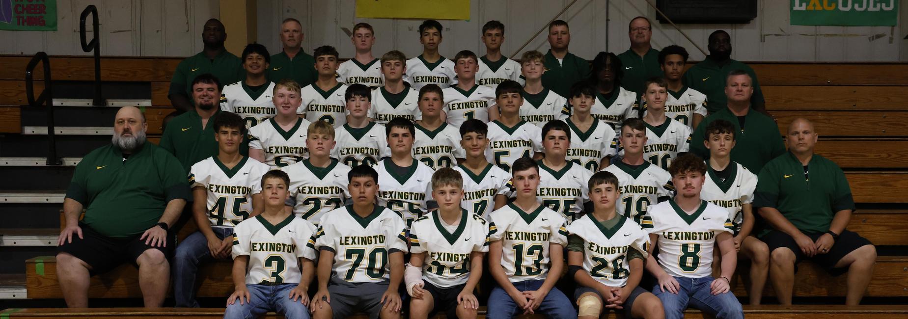 Football team posed together in uniforms with coaches on bleachers.