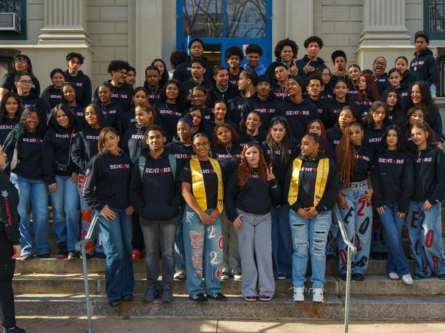 A large group of high school seniors posing together on stairs, wearing matching hoodies.