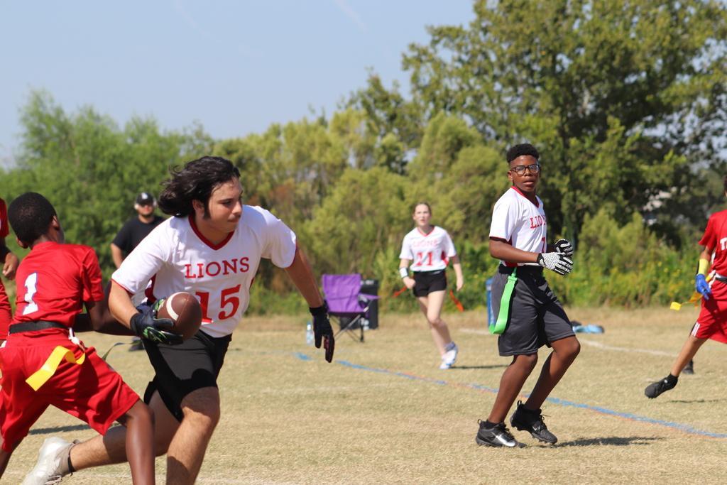 A student holds a football and runs to the right while others look on