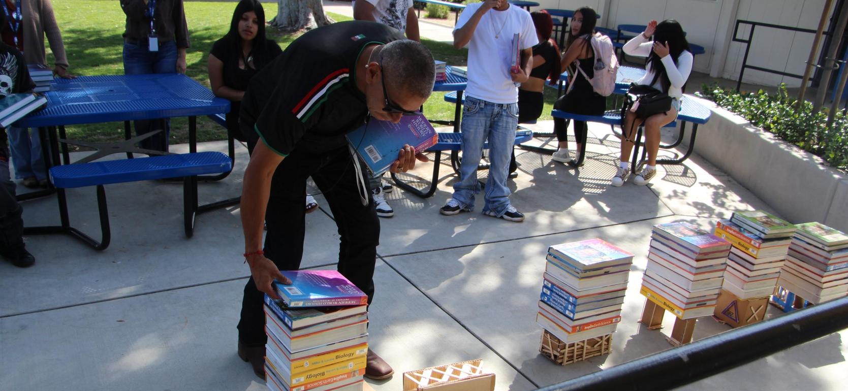 A person stacking books on a table, surrounded by others observing.