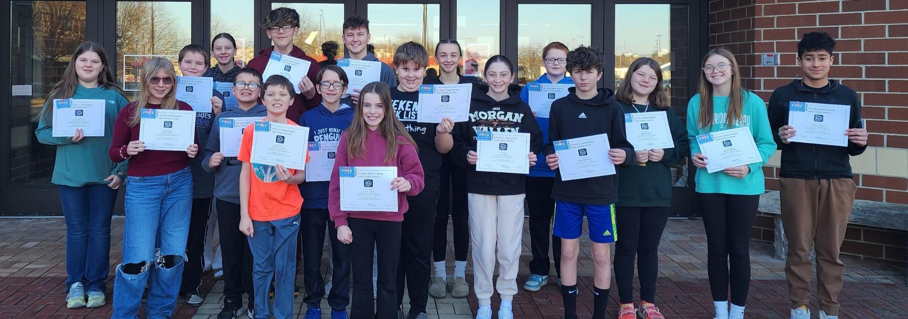 Group of students posing with certificates outside a school building.