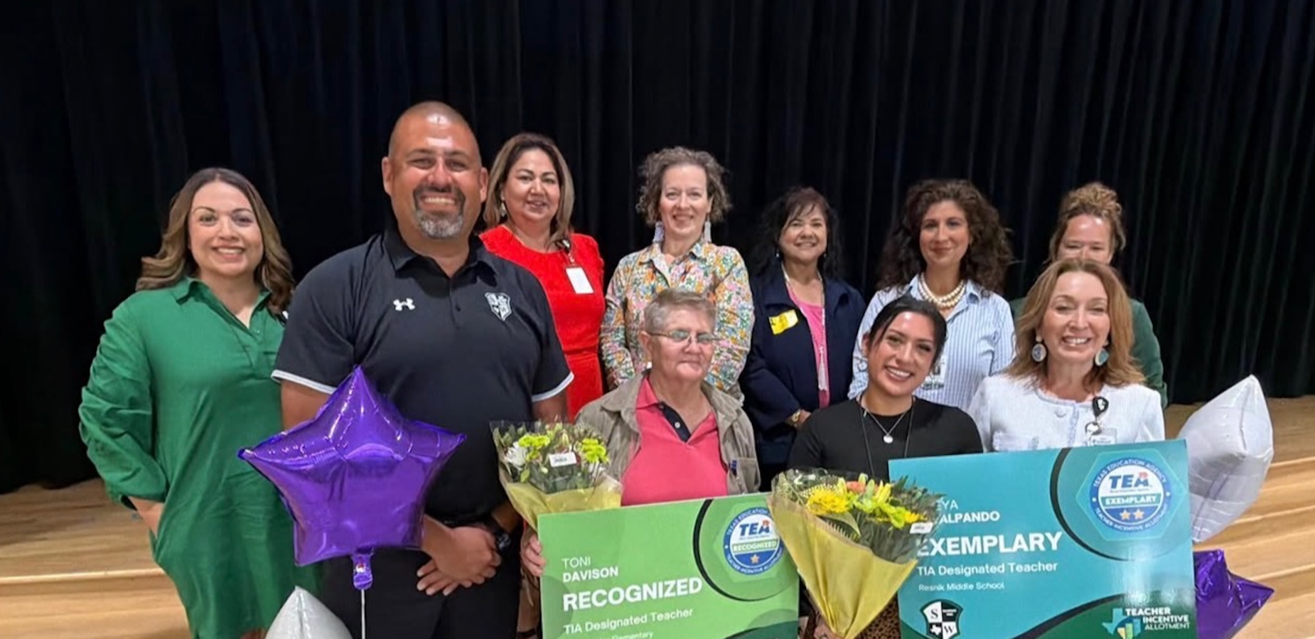 Group of smiling individuals celebrating with balloons and banners for outstanding teachers.