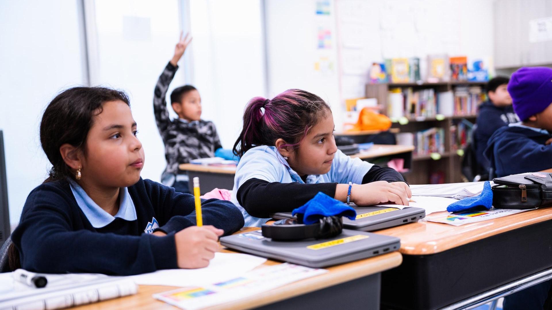 Two girls in a classroom working on assignments at their desks.
