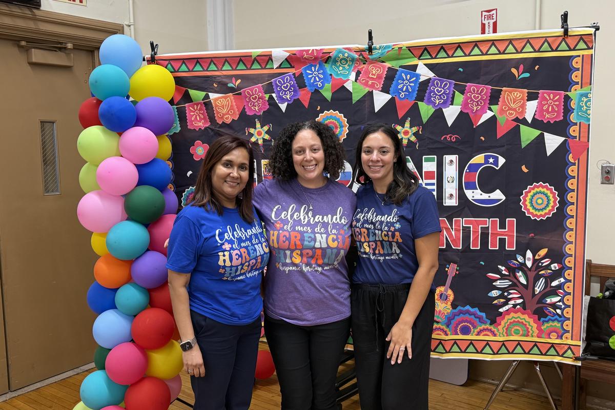 Three women posing in T-shirts for Hispanic Heritage Month with colorful decorations.