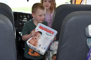 A boy holding a pack of Huggies diapers inside a vehicle.
