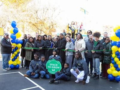 A ribbon-cutting ceremony with community members and leaders around a sign for a new space.