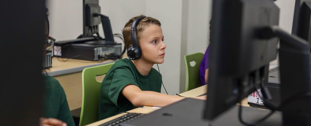 A boy wearing headphones focuses intently on a computer screen during a class.