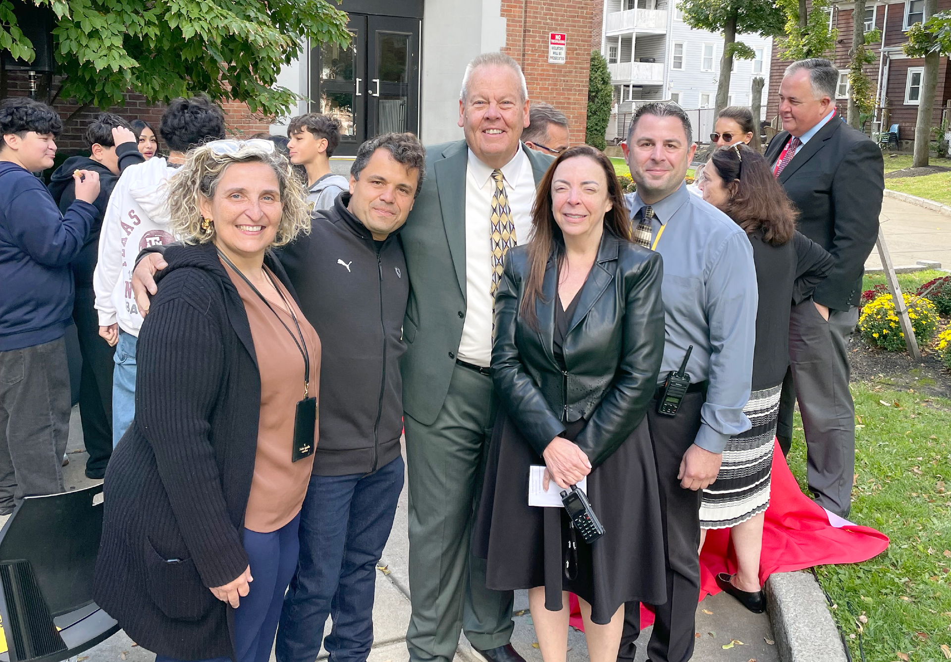 Group of six smiling people outdoors, standing together in a park.