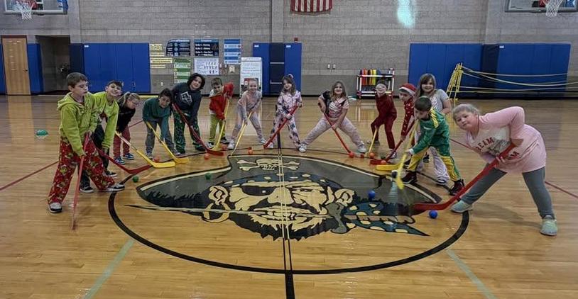 Children playing floor hockey in colorful pajamas on a gymnasium court.