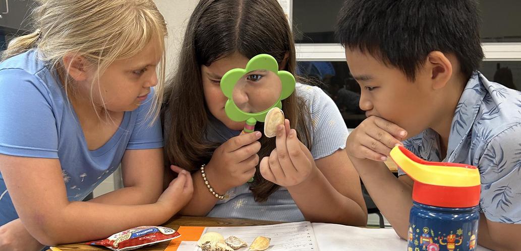 three students examining a shell with a magnifying glass
