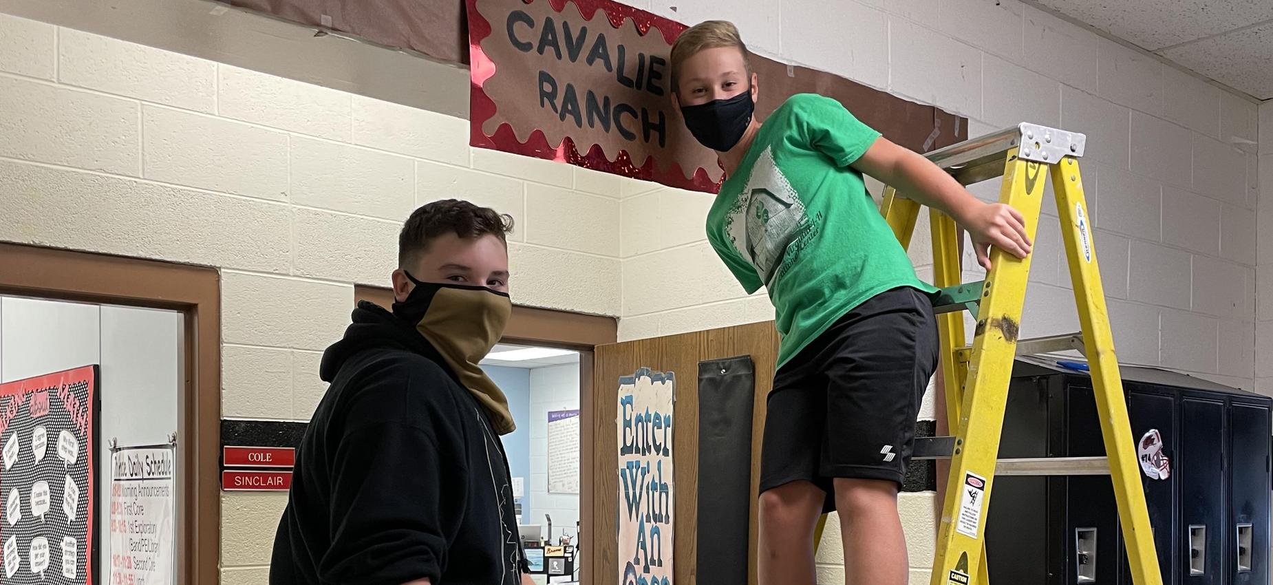 Two students stand on ladders in front of a classroom.