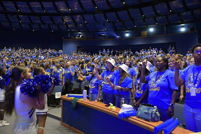 Cheerleaders in front of an auditorium of people singing the school song