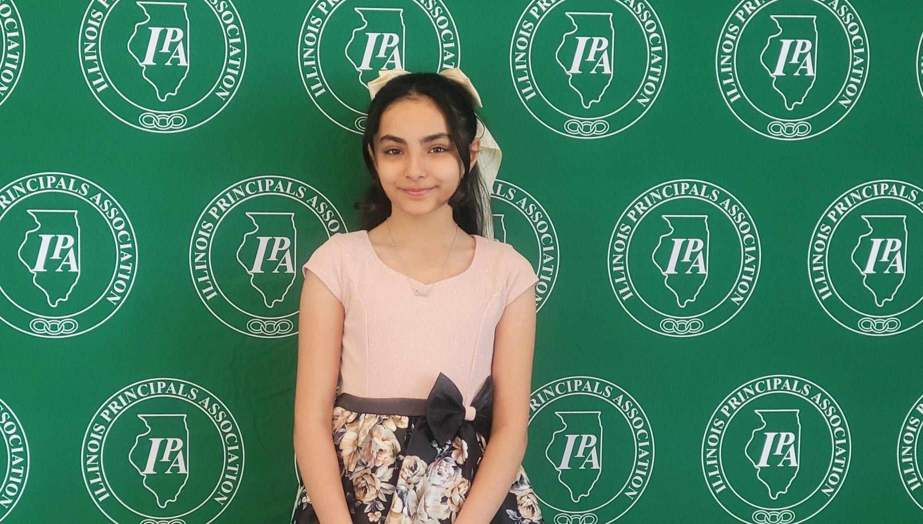 A young girl in a floral dress stands against a green backdrop with logos.