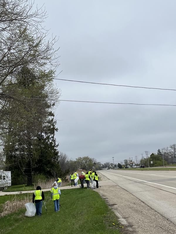 Group of volunteers with trash bags alongside a road on a cloudy day.