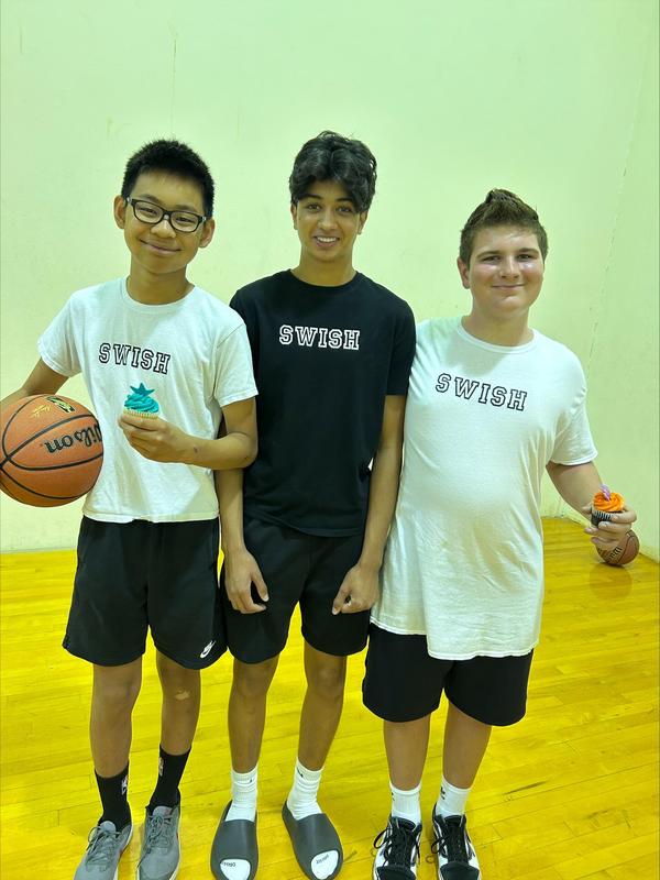 two students stand with Krish Parikh on the basketball court.