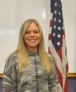 Blonde woman in a sweater poses with an American flag.
