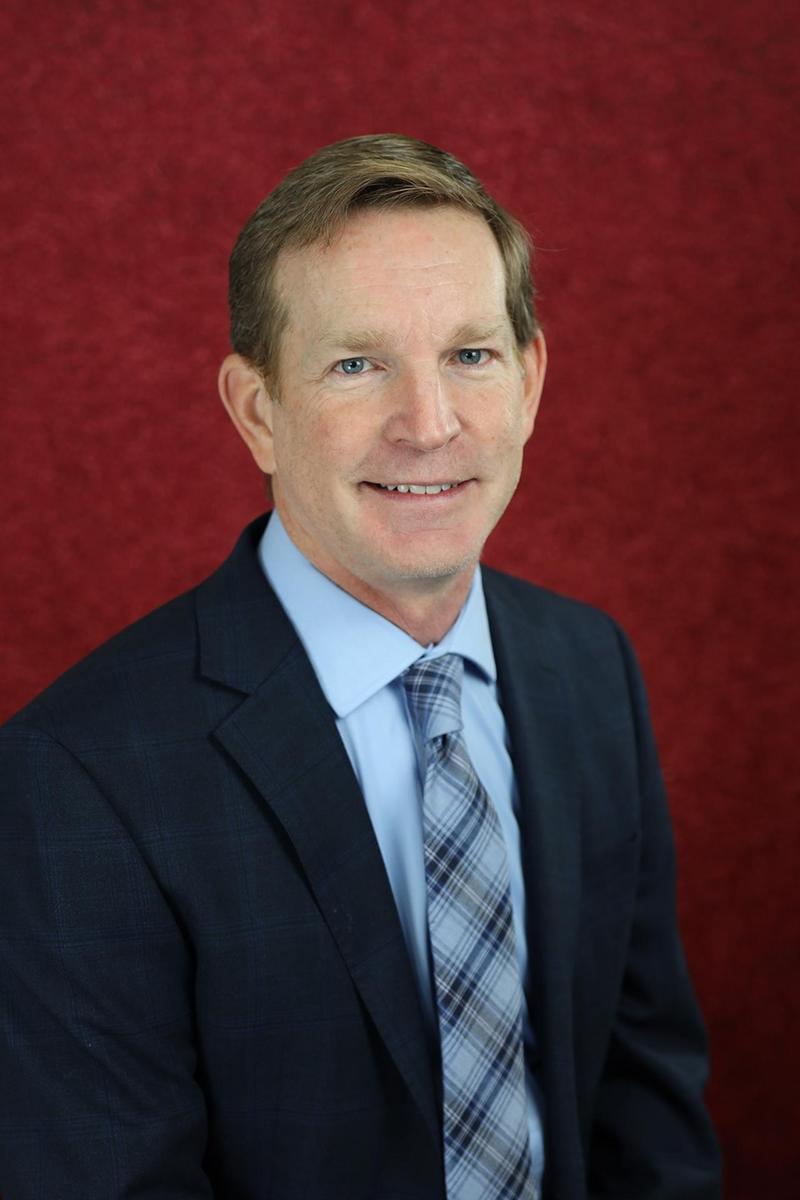 Smiling man in a checked shirt against a red background.