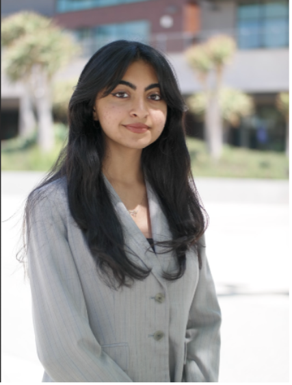 A young woman in a light gray blazer posing outdoors.