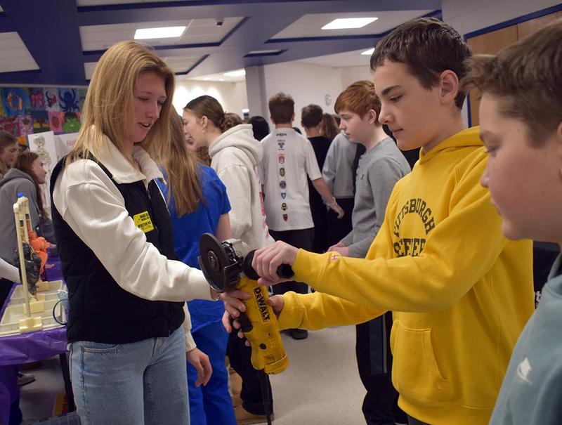 a girl showing a boy how to use a cordless grinder